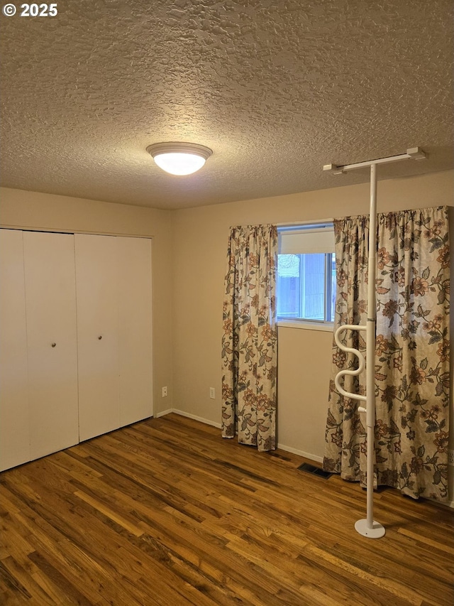 unfurnished bedroom featuring a textured ceiling, visible vents, wood finished floors, and a closet