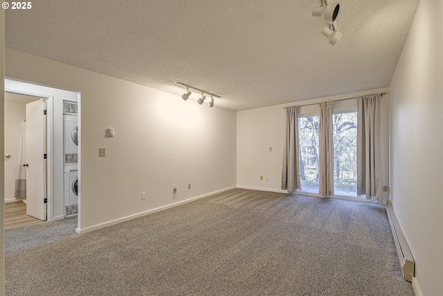 carpeted spare room with stacked washer / dryer, rail lighting, a textured ceiling, and a baseboard heating unit