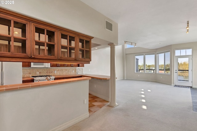 kitchen featuring decorative columns, backsplash, stove, light colored carpet, and tile counters