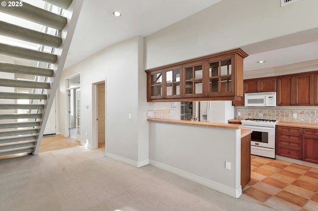 kitchen featuring white appliances, kitchen peninsula, light colored carpet, and decorative backsplash