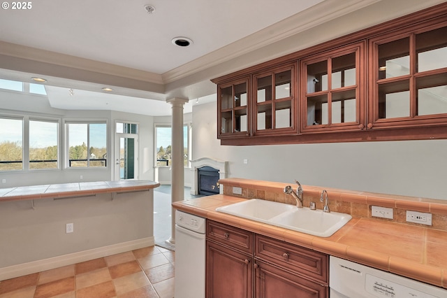 kitchen featuring sink, dishwasher, decorative columns, tile counters, and ornamental molding