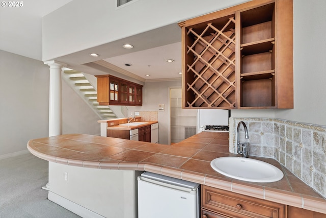 kitchen with tile countertops, decorative columns, sink, carpet flooring, and kitchen peninsula