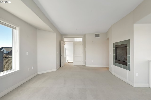 empty room featuring a tiled fireplace and light carpet