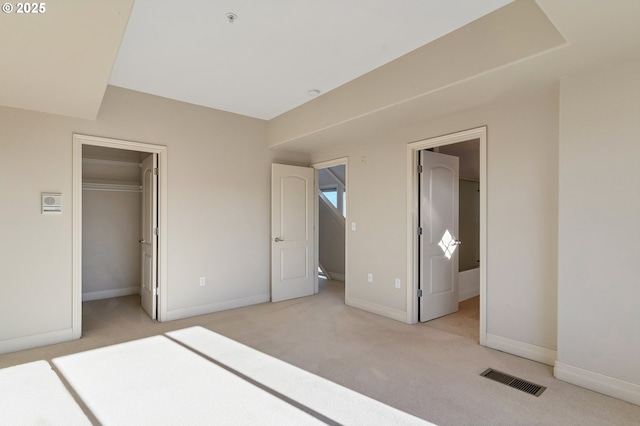 unfurnished bedroom with a closet, ensuite bathroom, a spacious closet, and light carpet