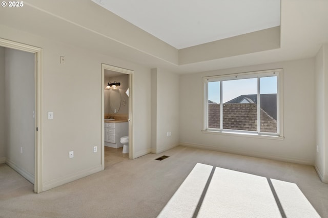 unfurnished bedroom featuring light carpet, a tray ceiling, and ensuite bathroom