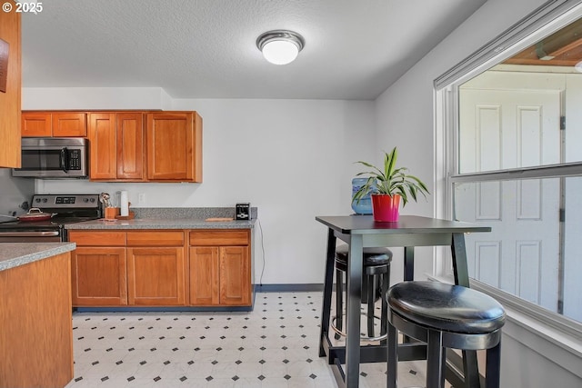 8458 SW Mohawk St, Tualatin, OR 97062 - kitchen featuring stainless steel microwave, range with electric cooktop, brown cabinets, light flooring, and dark countertops