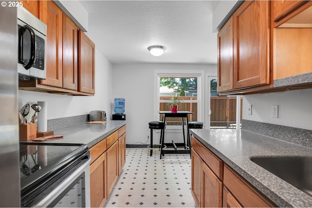 8458 SW Mohawk St, Tualatin, OR 97062 - kitchen featuring stainless steel appliances, light flooring, brown cabinetry, and a textured ceiling
