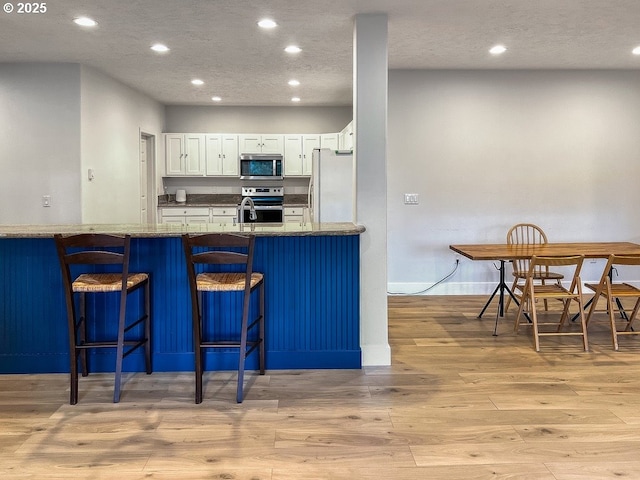 1500 SW Miller Ct, Gresham, OR 97080 - kitchen featuring appliances with stainless steel finishes, recessed lighting, light wood-style floors, a breakfast bar area, and white cabinets