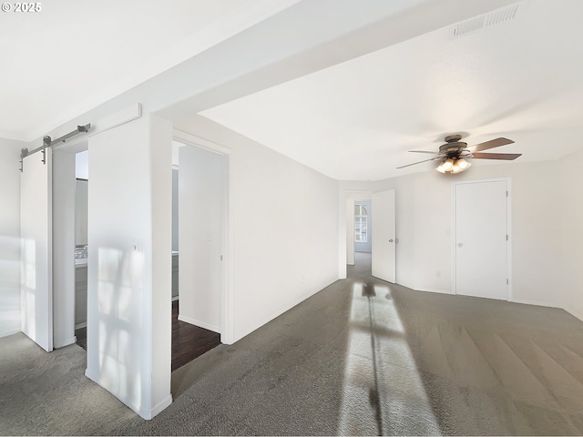 carpeted empty room with a barn door, visible vents, and a ceiling fan