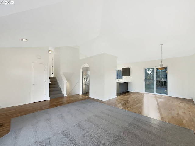 unfurnished living room featuring arched walkways, lofted ceiling, stairway, and wood finished floors