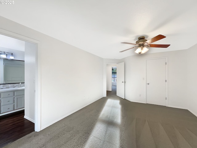 spare room featuring a ceiling fan, baseboards, dark carpet, and a sink