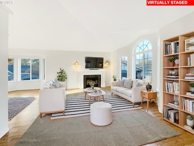 living area featuring lofted ceiling, plenty of natural light, wood finished floors, and a tile fireplace