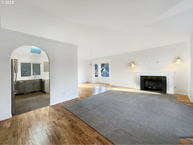 unfurnished living room with a sink, arched walkways, a tiled fireplace, and wood finished floors