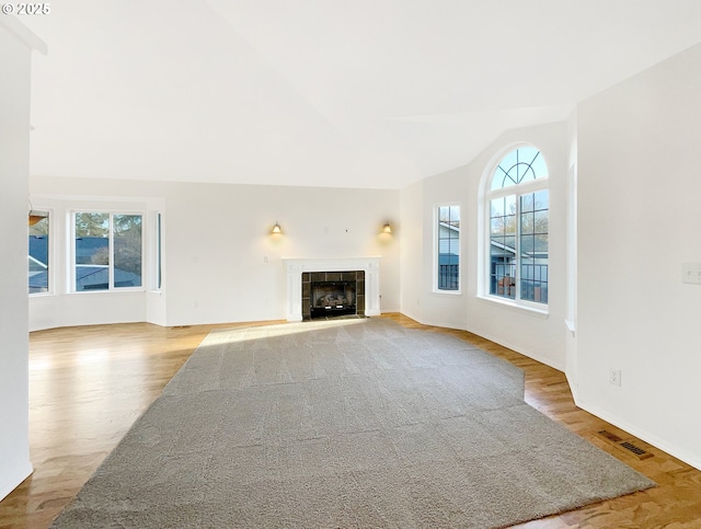 unfurnished living room with plenty of natural light, visible vents, vaulted ceiling, and a tiled fireplace