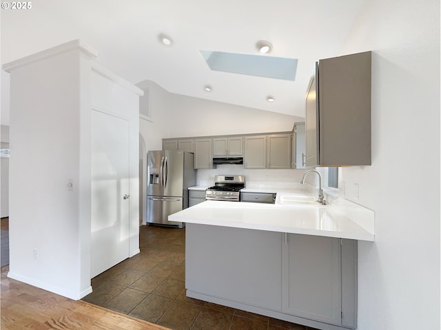 kitchen featuring appliances with stainless steel finishes, a peninsula, gray cabinets, under cabinet range hood, and a sink