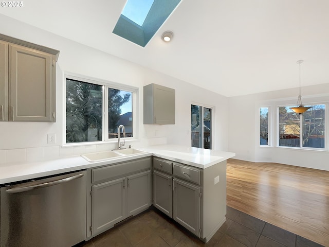 kitchen featuring a peninsula, stainless steel dishwasher, a sink, and gray cabinetry