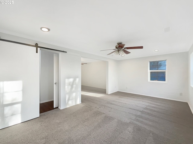 carpeted spare room with recessed lighting, ceiling fan, baseboards, and a barn door