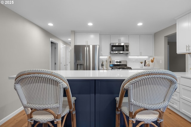 kitchen featuring appliances with stainless steel finishes, a kitchen bar, white cabinetry, backsplash, and light wood-type flooring