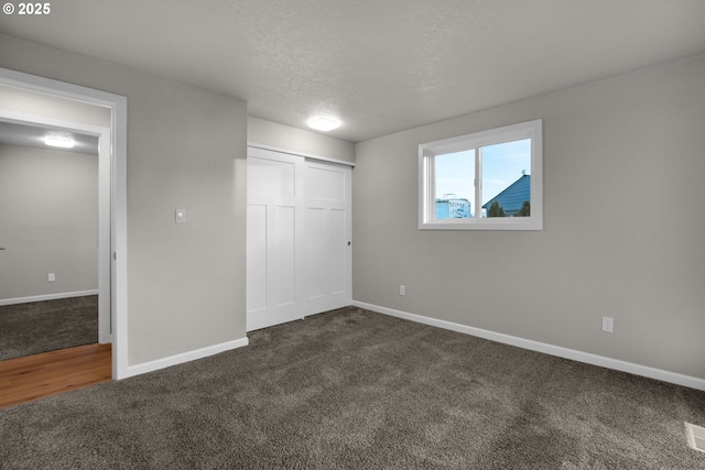 unfurnished bedroom with a closet, a textured ceiling, and dark colored carpet