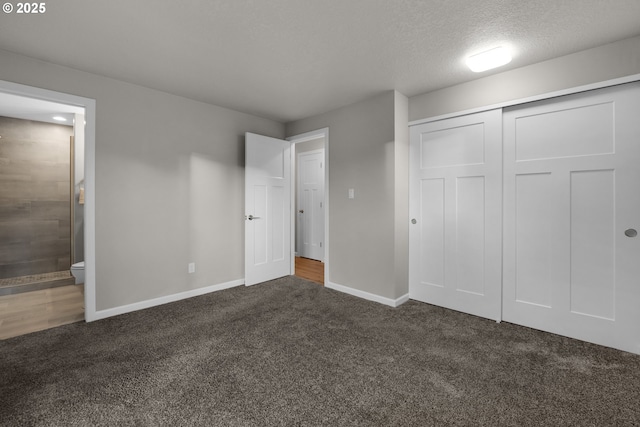 unfurnished bedroom featuring a textured ceiling, dark colored carpet, a closet, and connected bathroom