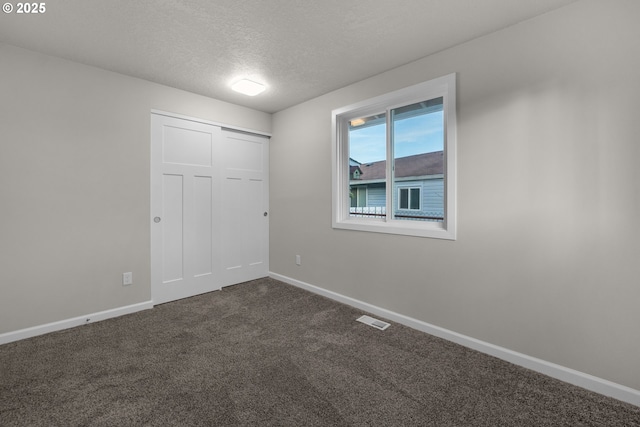 unfurnished bedroom featuring a textured ceiling, a closet, and dark carpet