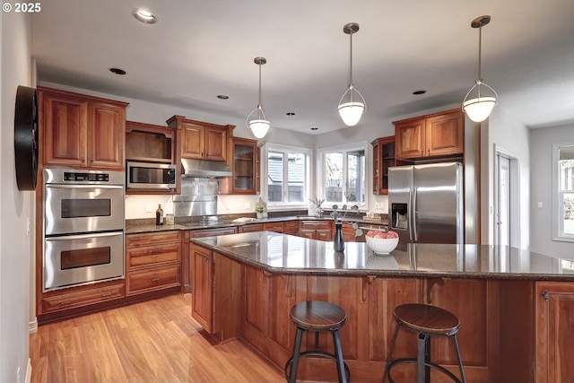 kitchen featuring a breakfast bar, decorative light fixtures, a center island, light hardwood / wood-style flooring, and appliances with stainless steel finishes