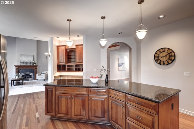 kitchen with light hardwood / wood-style flooring, a kitchen island, hanging light fixtures, and dark stone countertops