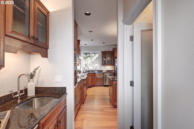 kitchen featuring light wood-type flooring, dishwasher, sink, and dark stone countertops