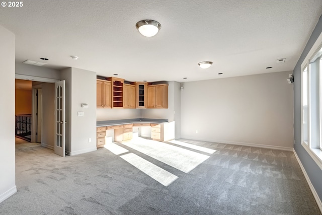 unfurnished living room with light carpet, built in desk, a textured ceiling, and plenty of natural light