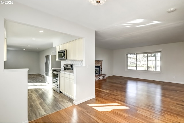 kitchen with light wood finished floors, backsplash, a brick fireplace, white cabinetry, and stainless steel appliances