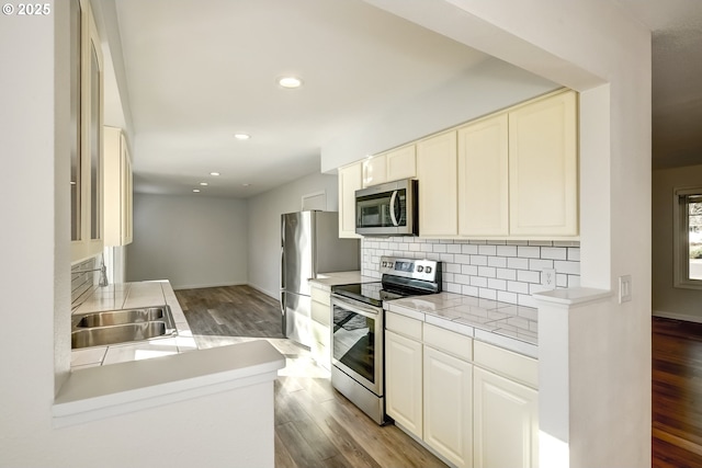 kitchen with a sink, decorative backsplash, light countertops, appliances with stainless steel finishes, and light wood-type flooring