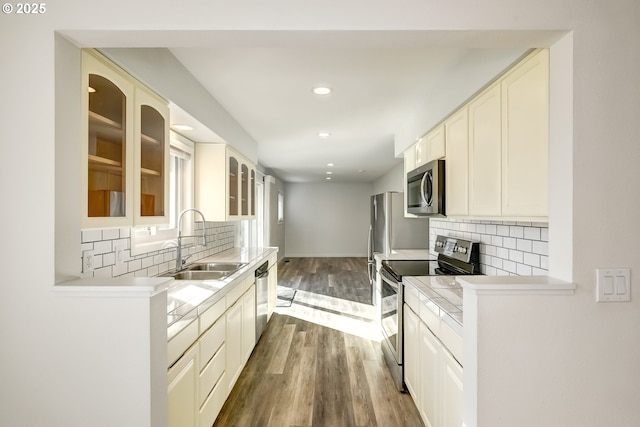 kitchen with dark wood finished floors, a sink, decorative backsplash, glass insert cabinets, and appliances with stainless steel finishes