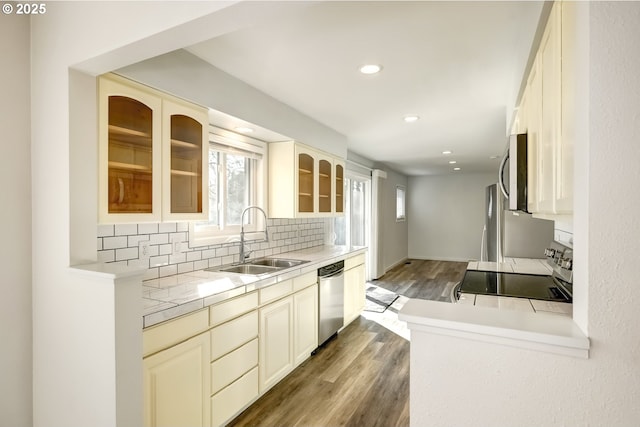 kitchen with a sink, backsplash, wood finished floors, stainless steel appliances, and glass insert cabinets