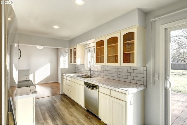 kitchen with a sink, backsplash, cream cabinets, dishwasher, and tile counters