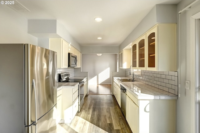 kitchen featuring light countertops, wood finished floors, cream cabinetry, stainless steel appliances, and a sink