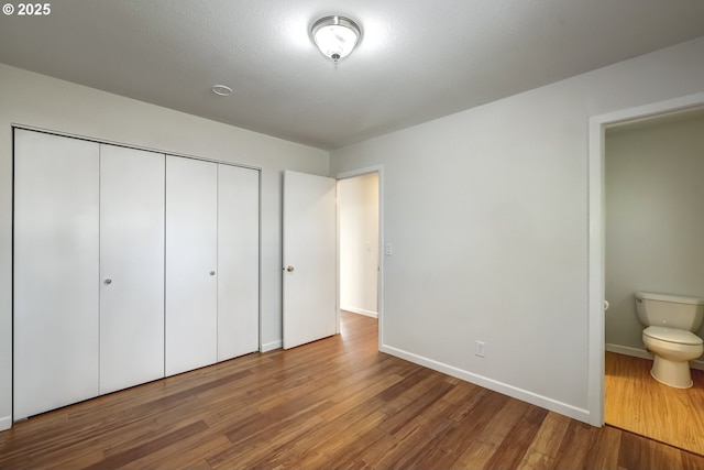 unfurnished bedroom featuring wood finished floors, a closet, and baseboards