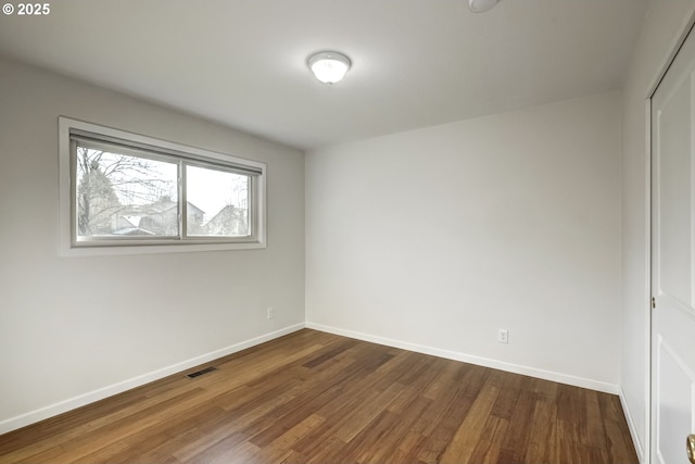 spare room featuring visible vents, baseboards, and dark wood-style flooring