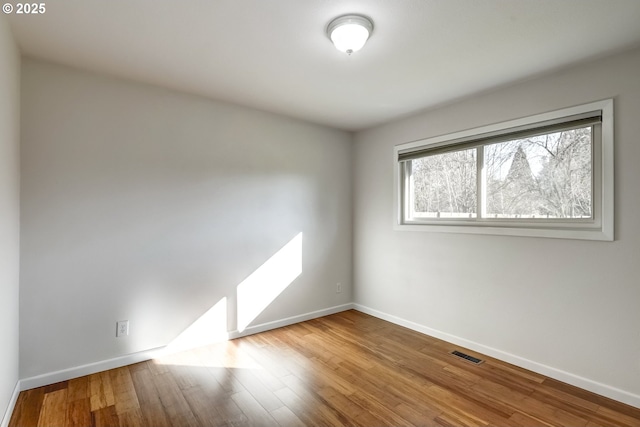 empty room featuring wood finished floors, visible vents, and baseboards