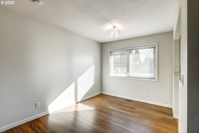 empty room with wood finished floors, visible vents, and baseboards