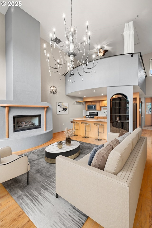 living room with light hardwood / wood-style flooring, a towering ceiling, and a notable chandelier