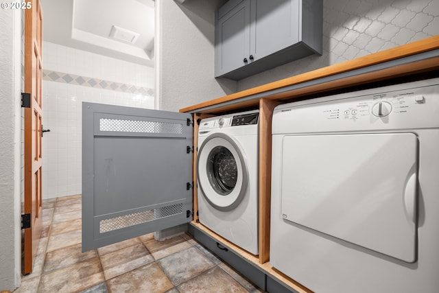 washroom with cabinets, washing machine and dryer, and tile walls