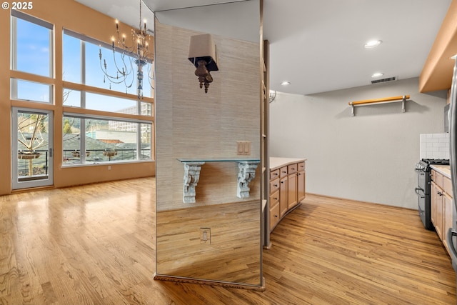 kitchen featuring light brown cabinets, black range with gas stovetop, a chandelier, pendant lighting, and light hardwood / wood-style floors