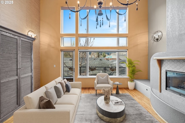 living room featuring a high ceiling, light hardwood / wood-style flooring, a tile fireplace, and an inviting chandelier