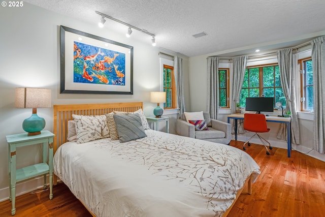 bedroom featuring a textured ceiling, wood finished floors, track lighting, a desk, and baseboards