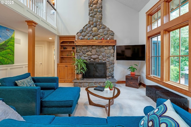 living area with a high ceiling, carpet flooring, a stone fireplace, and ornate columns