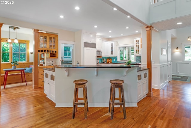kitchen featuring dark countertops, a kitchen bar, light wood-type flooring, white cabinets, and recessed lighting