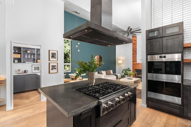 5210 SW Hewett Blvd, Portland, OR 97221 - kitchen featuring island range hood, appliances with stainless steel finishes, a towering ceiling, a ceiling fan, and a glass covered fireplace