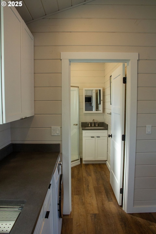 interior space featuring washer / dryer, wooden walls, dark countertops, dark wood-type flooring, and white cabinetry