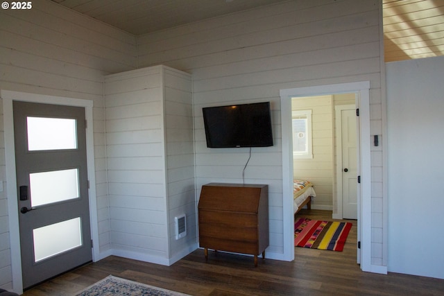 foyer entrance with visible vents, dark wood finished floors, and wooden walls