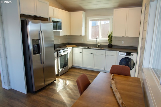 kitchen with dark wood finished floors, dark countertops, washer / clothes dryer, appliances with stainless steel finishes, and a sink